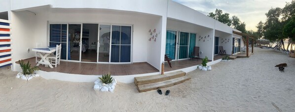 A modern beach house with a covered patio, a small garden, and a sandy beach area.