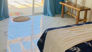 Een kamer met een bed, een tafeltje, een potplant en uitzicht op het strand door een glazen deur.