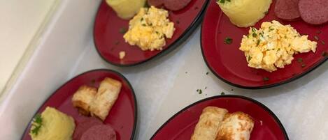 A tray of food items including scrambled eggs, sausage slices, and a pastry on a red plate.
