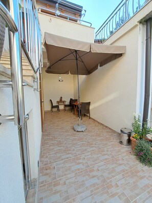 A patio area with a table and chairs, a large umbrella, and a potted plant. - Studio Leo Apartment (Novigrad)