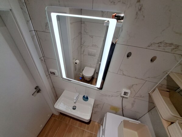A bathroom with a white sink, a mirror with LED lighting, a toilet, and a shower area.
