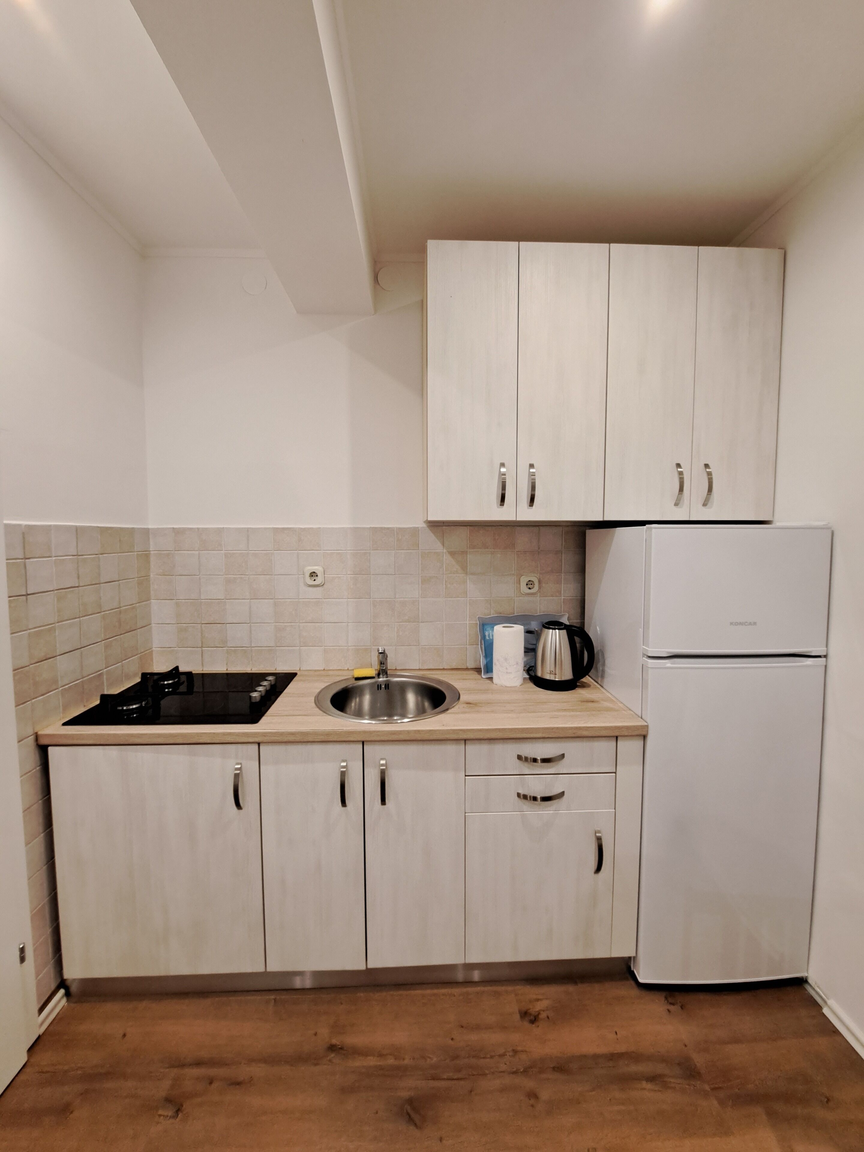 A compact kitchen with light wood cabinets, a stainless steel sink, a black stove, and a white refrigerator.