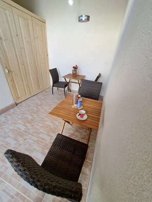 A small patio area with a wooden table and two wicker chairs, a potted plant, and a wall-mounted light fixture. - Studio Leo Apartment (Novigrad)