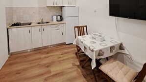 Ett kompakt kök med vita skåp, ett kylskåp, en diskho och ett bord med en duk på.