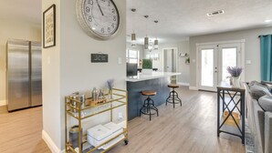 Une cuisine moderne avec un réfrigérateur en acier inoxydable, une grande horloge murale et un coin bar équipé de tabourets.