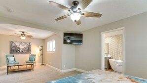 Une chambre à coucher comprenant un lit, un ventilateur de plafond, une télévision, une chaise et une salle de bain avec une baignoire.