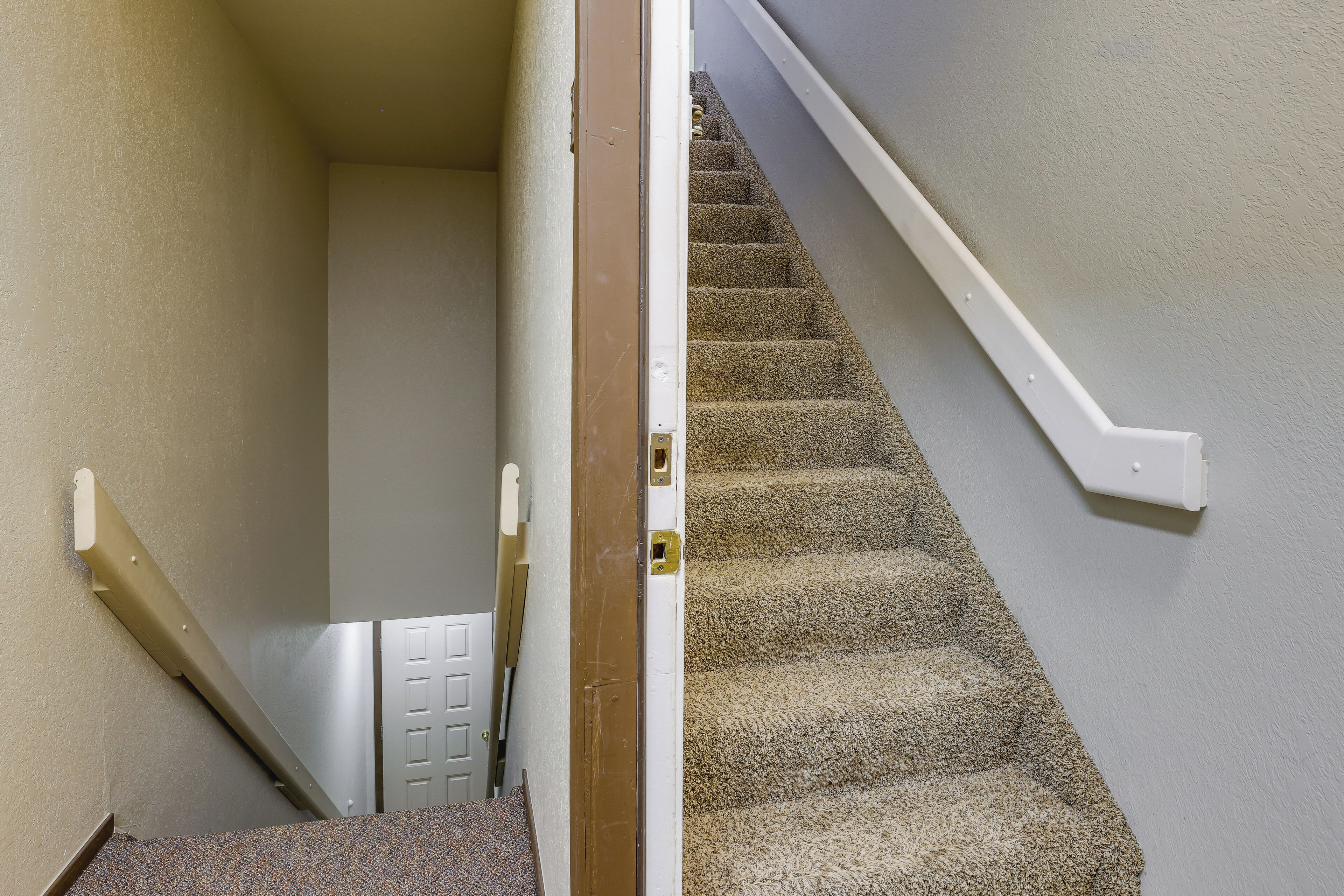 Una escalera alfombrada con barandilla blanca y una puerta al final.