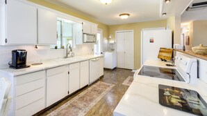 A modern kitchen with white cabinetry, a built-in microwave, a stove, and a coffee maker.