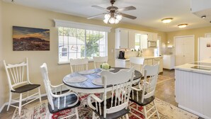 A kitchen with white cabinetry, a dining table with white chairs, and a ceiling fan.