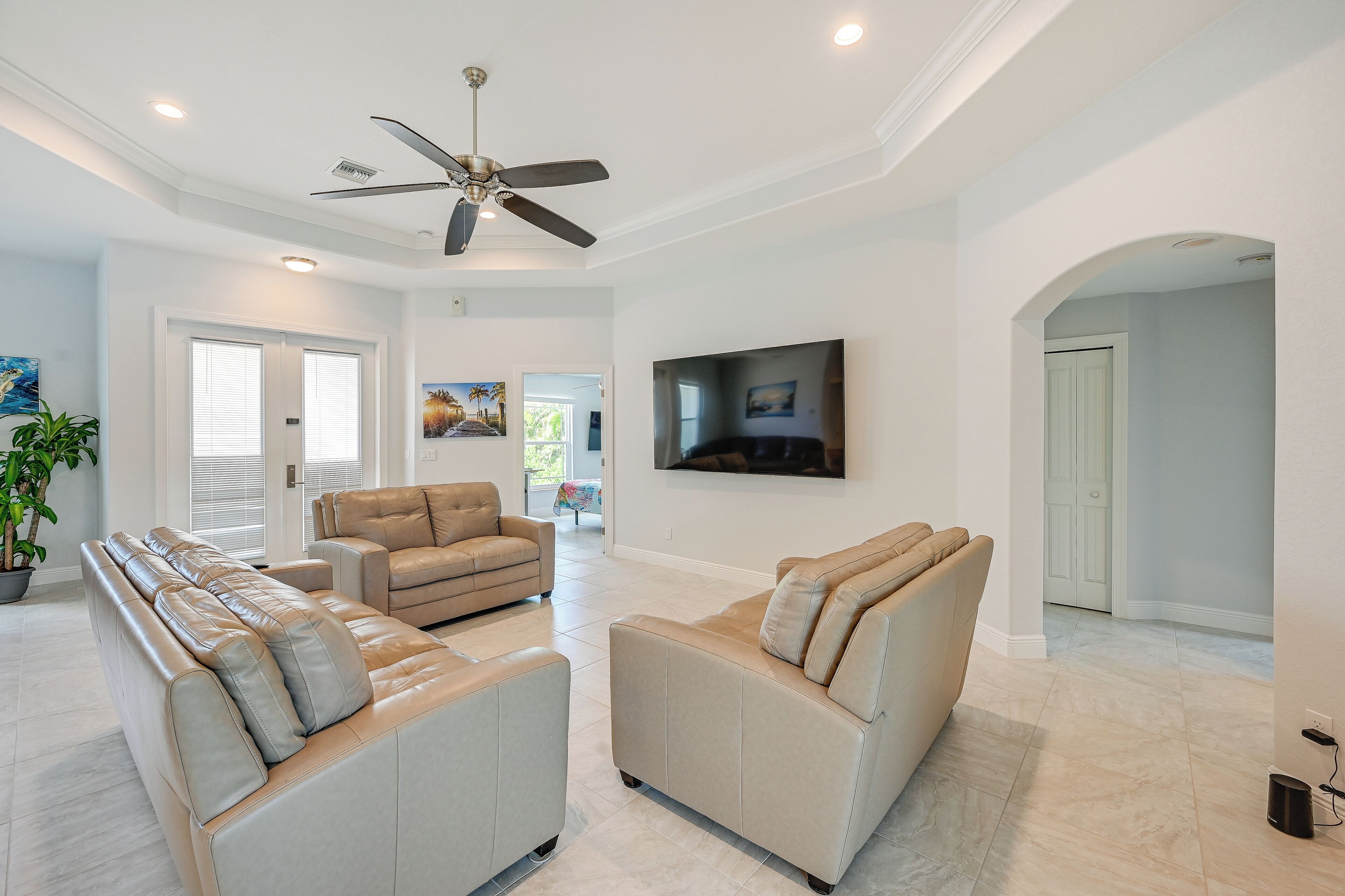 A spacious living room with a ceiling fan, a large flat-screen TV, and a beige sectional sofa.
