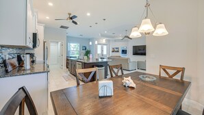 Una cocina moderna con armarios blancos, encimera de granito y comedor con mesa y sillas de madera.