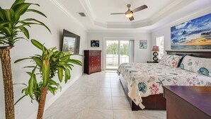 Un dormitorio con una cama, ventilador de techo, un ventanal grande y un cuadro en la pared.