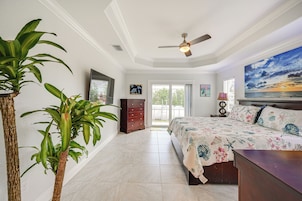 A bedroom with a bed, a ceiling fan, a large window, and a painting on the wall.