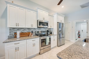 A modern kitchen with white cabinets, stainless steel appliances, granite countertops, and a tiled backsplash.