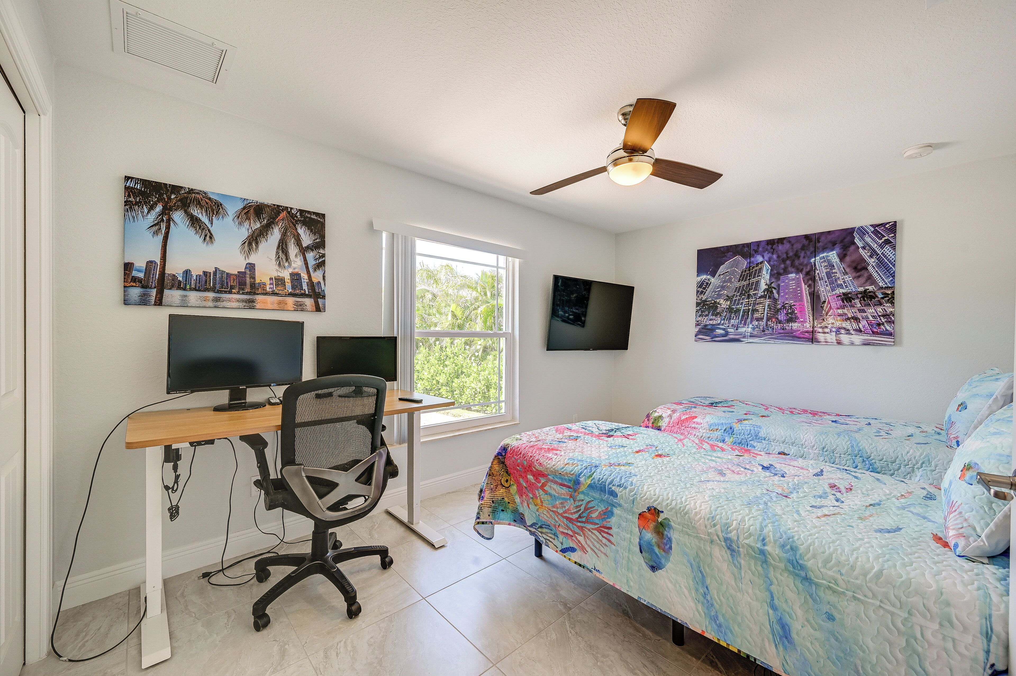 A bedroom with a bed, a desk with a computer, and two wall-mounted TVs.