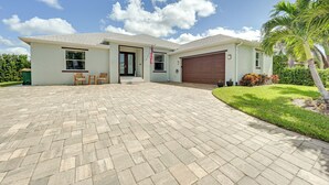 Una casa de dos pisos con entrada pavimentada, un garaje y un pequeño patio con sillas.
