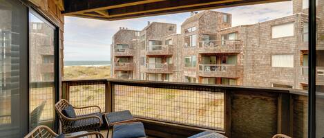 Een balkon met rieten meubels, een glazen tafel en uitzicht op een bakstenen gebouw met balkons.