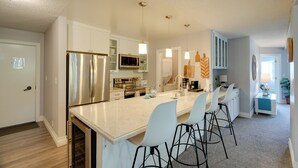 A modern kitchen with white cabinetry, stainless steel appliances, and a central island with bar stools. - Oceanfront Watsonville Condo w/ Beach Access! (Watsonville)