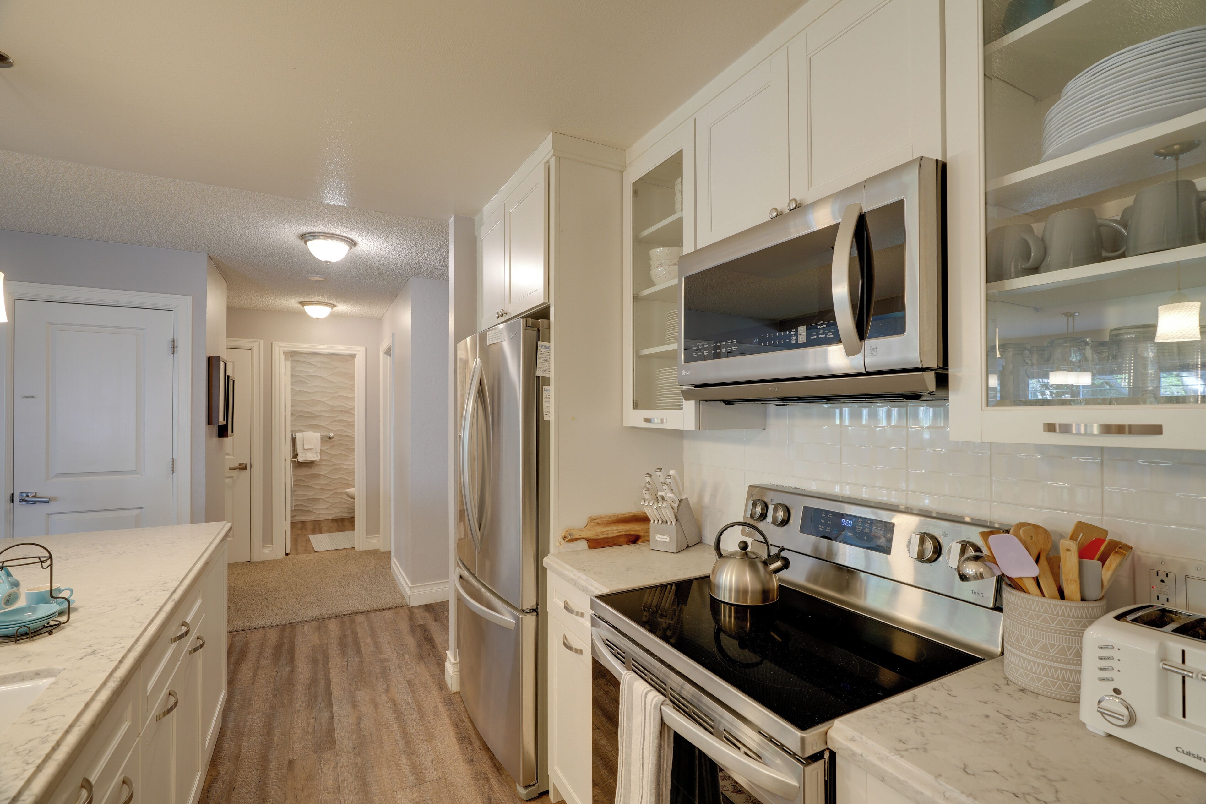 A modern kitchen with white cabinetry, stainless steel appliances, and a marble countertop.