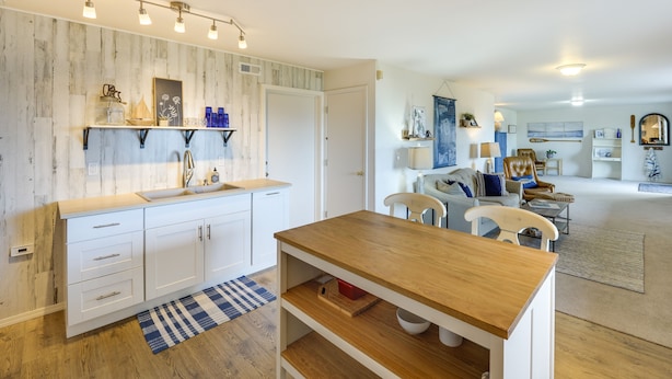 A modern kitchen with white cabinetry, a wooden countertop, and a built-in sink. There is a dining area with a wooden table and chairs, and a living room with a sofa and a coffee table.