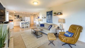 A modern living room with a sofa, armchair, coffee table, and a dining area in the background.