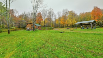 A rustic cabin with a green roof, surrounded by a grassy field and trees with autumn foliage.