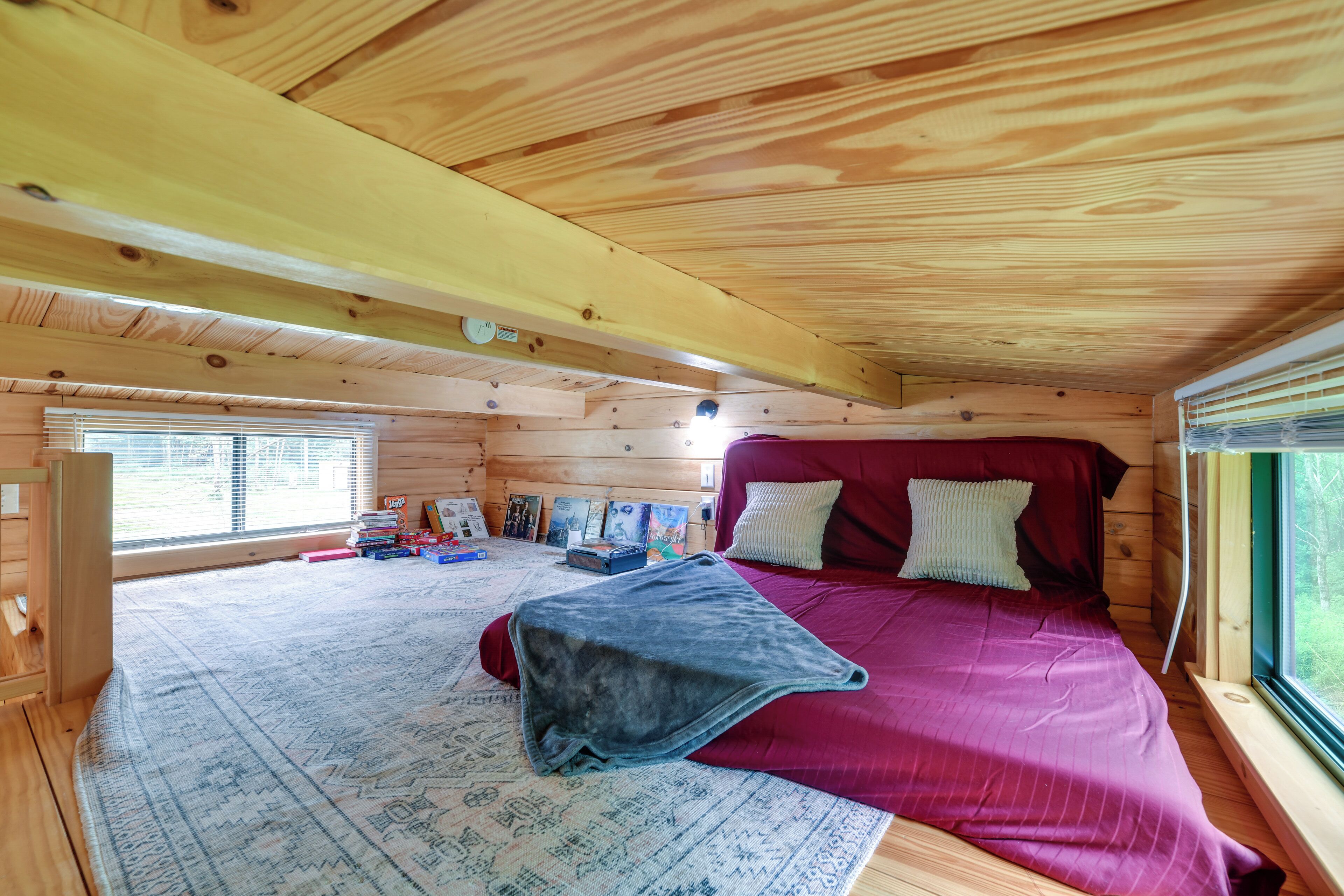 Interior de una cabaña de madera con una cama, un tapete y una ventana.