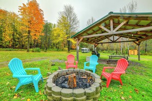 A covered outdoor seating area with Adirondack chairs and a fire pit. - Catskills Tiny Home Cabin: Surrounded by Nature! (Sidney Center)