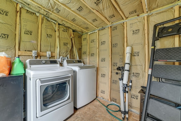 A laundry room with two washing machines and a dryer, surrounded by insulation and construction materials.