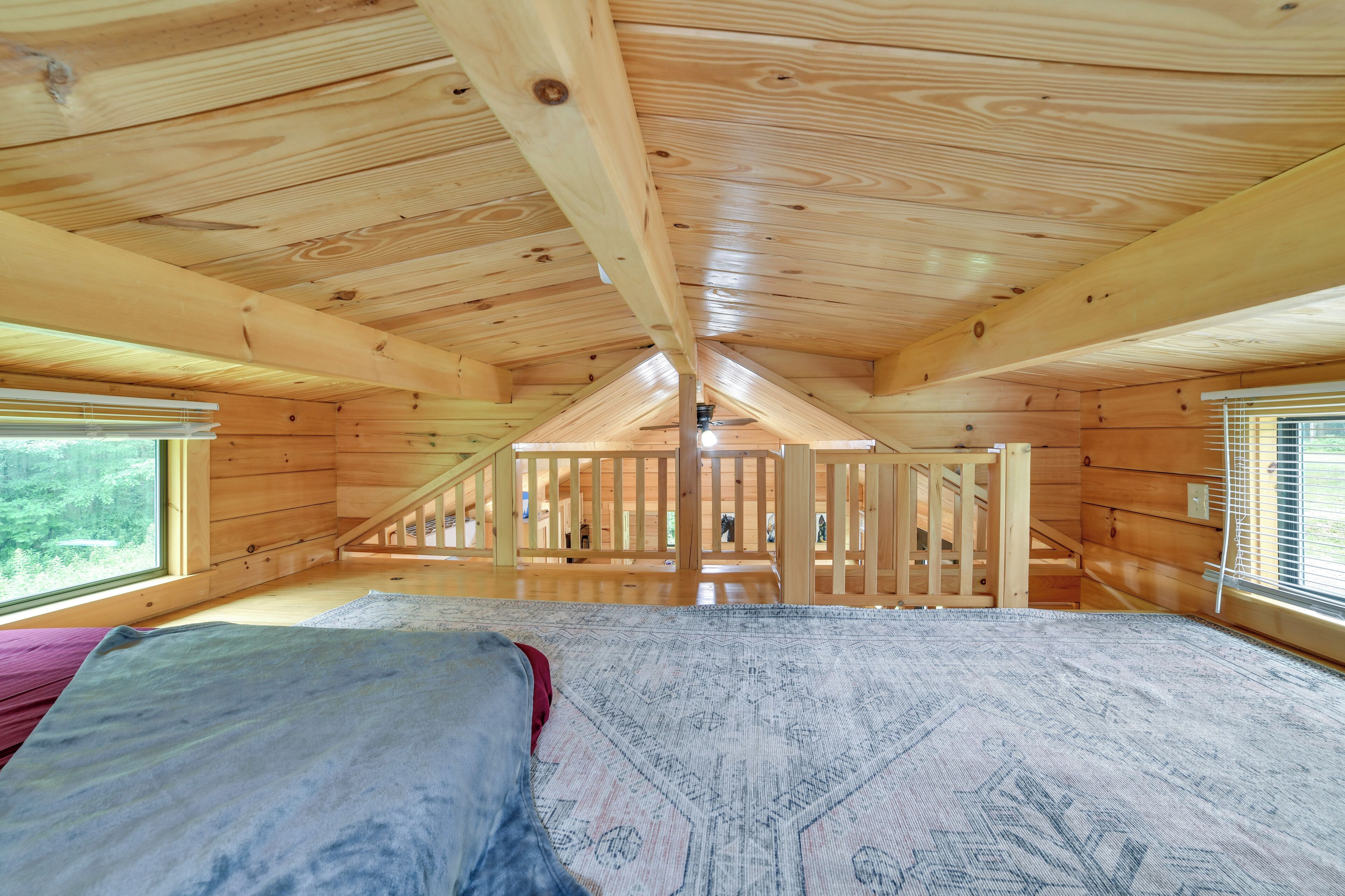 A wooden cabin with a loft bedroom, a staircase, and large windows.