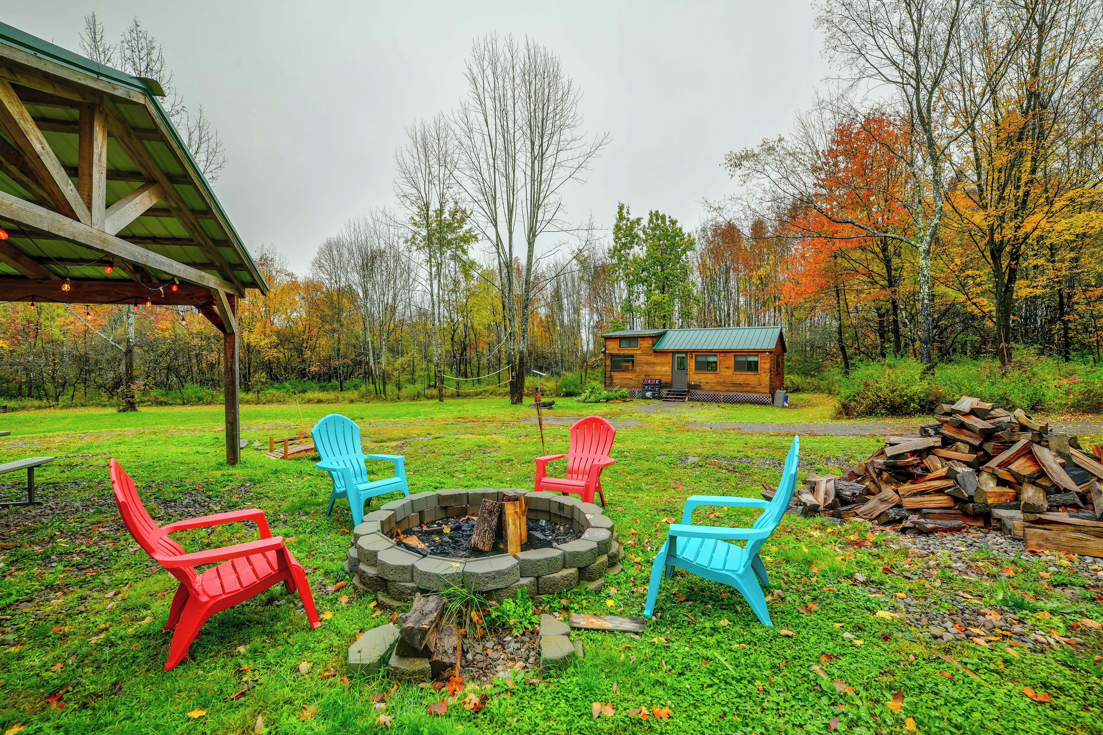 Une cabane rustique avec un foyer et des fauteuils Adirondack aux couleurs vives, située dans un espace boisé.