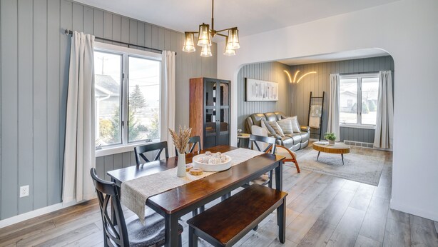 A dining area with a wooden table, chairs, and a chandelier. There is a sofa and a coffee table in the background. - Steps to Lake Michigan: Manitowoc Home w/ Fire Pit (Manitowoc)