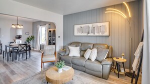 A modern living room with a grey sofa, a dining area, and a kitchen in the background. - Steps to Lake Michigan: Manitowoc Home w/ Fire Pit (Manitowoc)