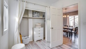 A room with a wooden floor, a white dresser, a laundry basket, and a door leading to a dining area with a table and chairs. - Steps to Lake Michigan: Manitowoc Home w/ Fire Pit (Manitowoc)