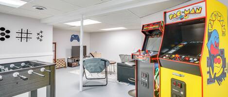 Et værelse med et bordfodboldbord, en Pac-Man arkademaskine og en dartskive på væggen.