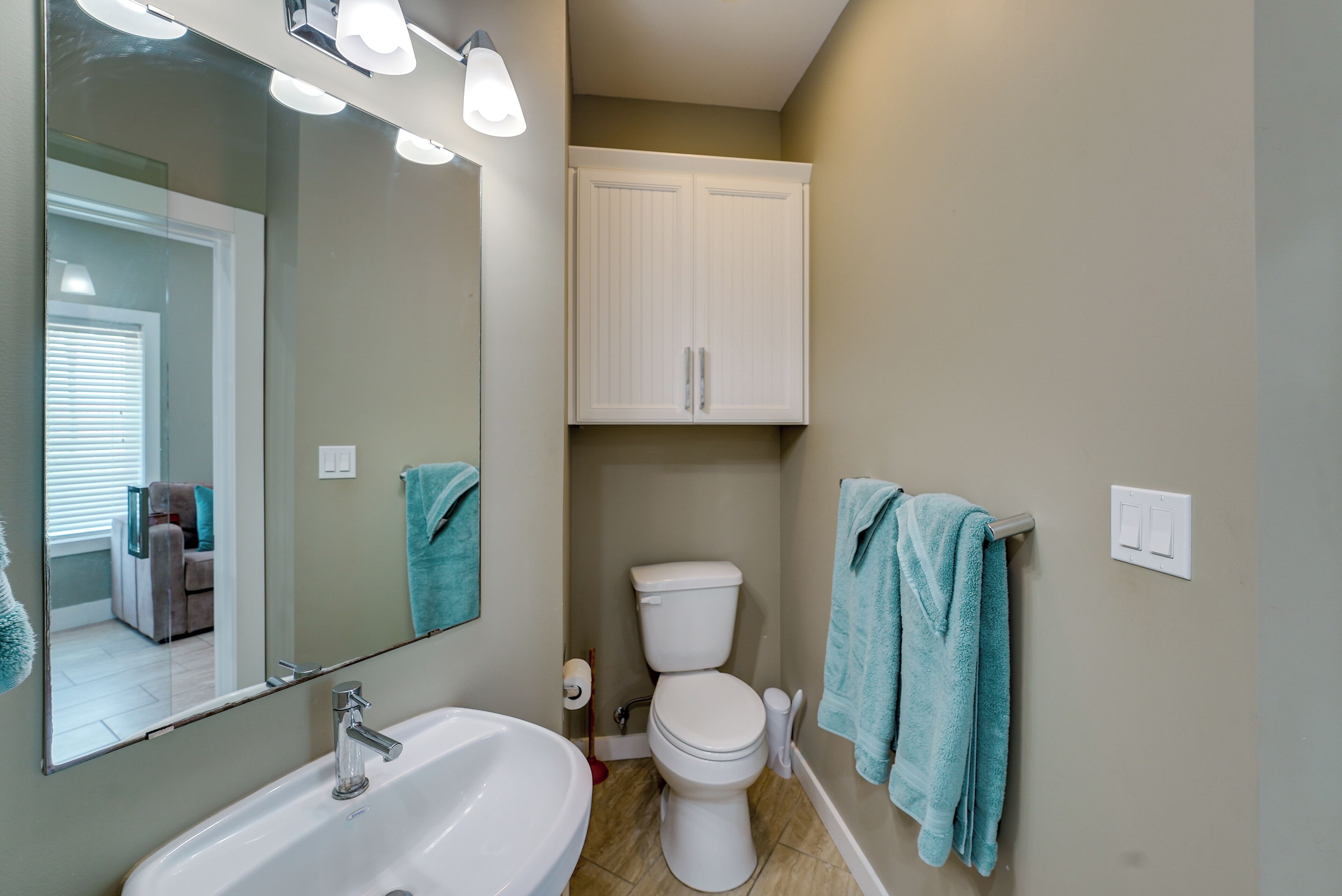 A bathroom with a white sink, a toilet, and a cabinet above the toilet. There are two towels hanging on the wall.