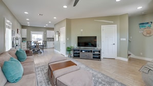 A spacious living room with a large TV, a sofa, and a dining area in the background. - Bright, Modern Corpus Christi Condo: 2 Mi to Beach (Corpus Christi)