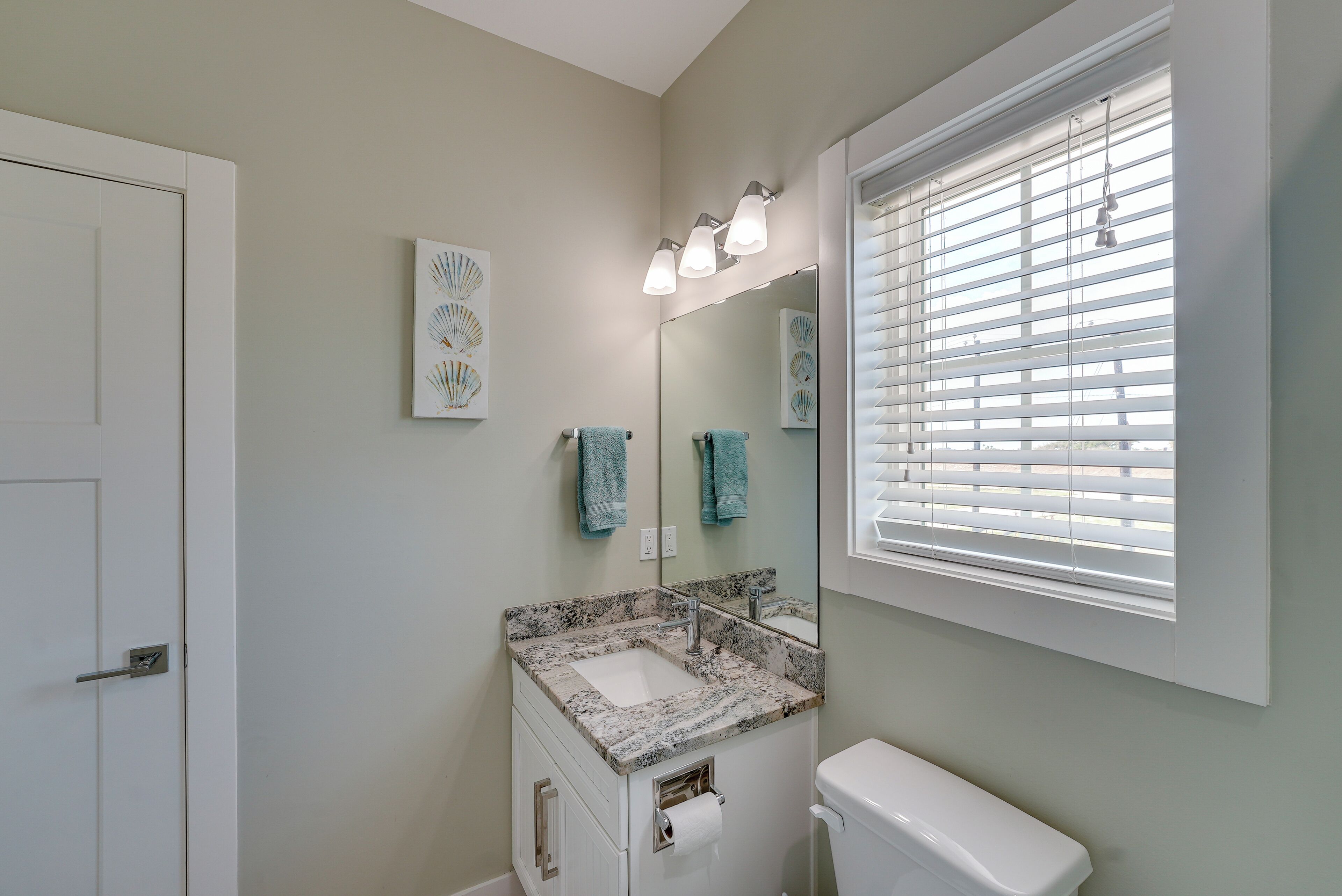 A bathroom with a white sink, a toilet, a mirror, and a window with blinds.