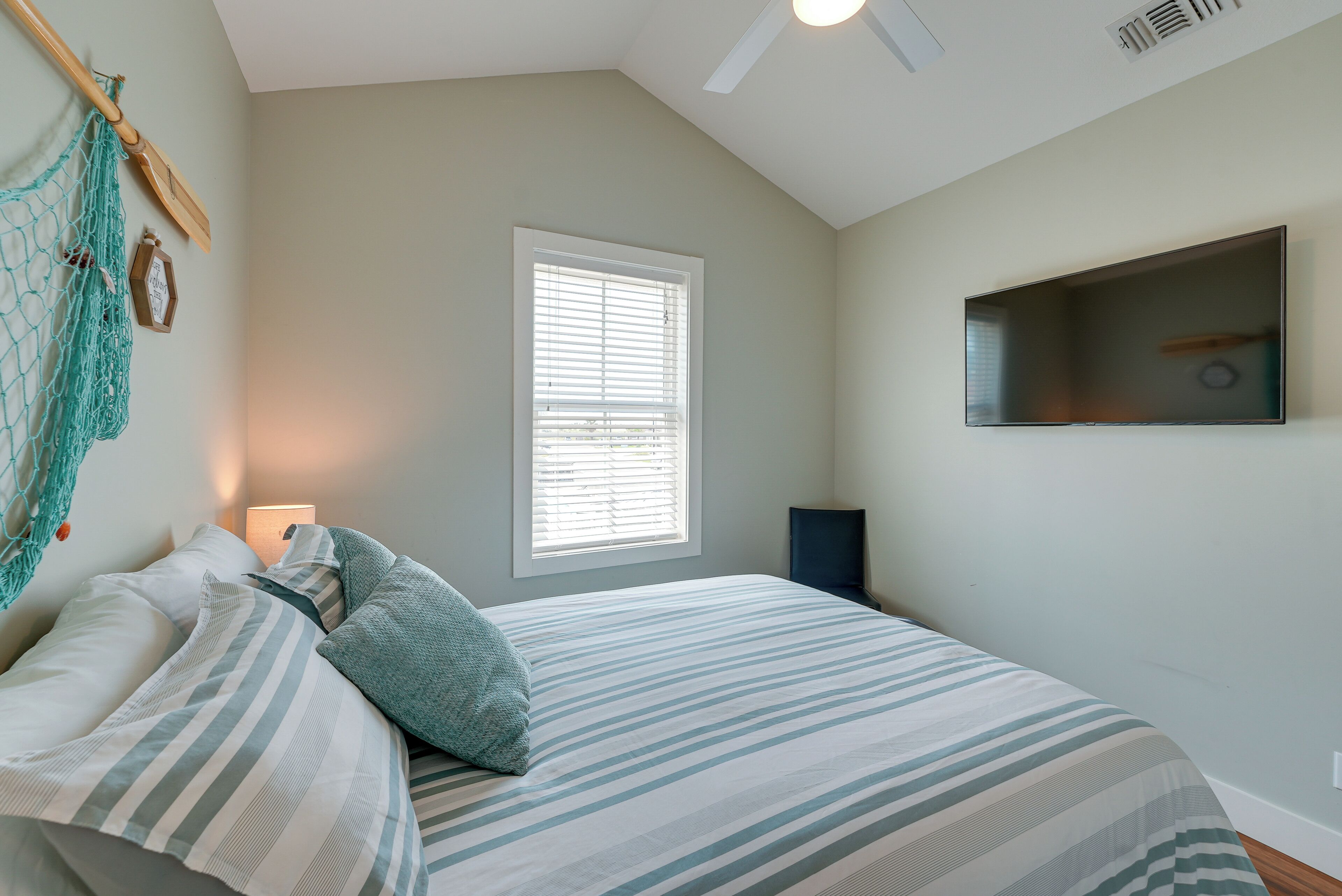 Un dormitorio con cama, ventana con persianas, una hamaca colgante y televisor montado.