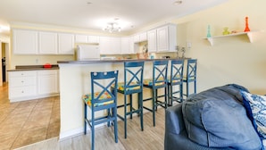 A kitchen with white cabinets, a central island with bar stools, and a ceiling fan. - Oak Island Vacation Rental ~ 1 Block to Beach! (Oak Island)