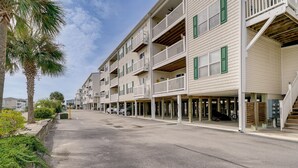 A row of beachfront condominiums with balconies, a clear sky, and a palm tree. - Oak Island Vacation Rental ~ 1 Block to Beach! (Oak Island)