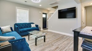 A modern living room with a blue sofa, glass coffee table, and a flat-screen TV mounted on the wall. - Updated Home - Walk to Salisbury University! (Salisbury)