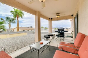 Eine überdachte Terrasse im Freien mit Tisch, Stühlen, einem Grill und Palmen im Hintergrund.