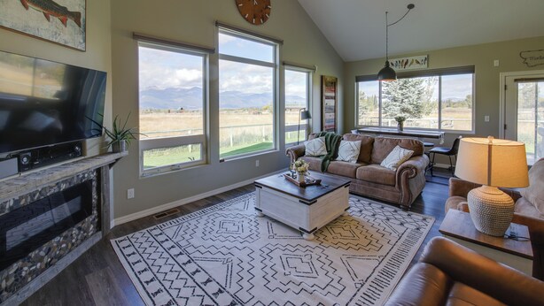 A spacious living room with a large TV, a fireplace, a couch, and a view of the mountains. - Pet-friendly Stevensville Home w/ Mountain Views! (Stevensville)