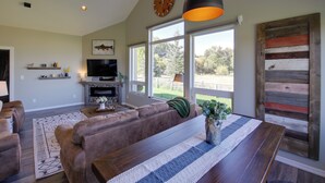 A spacious living room with a large window, a fireplace, a television, and a dining area with a wooden table. - Pet-friendly Stevensville Home w/ Mountain Views! (Stevensville)