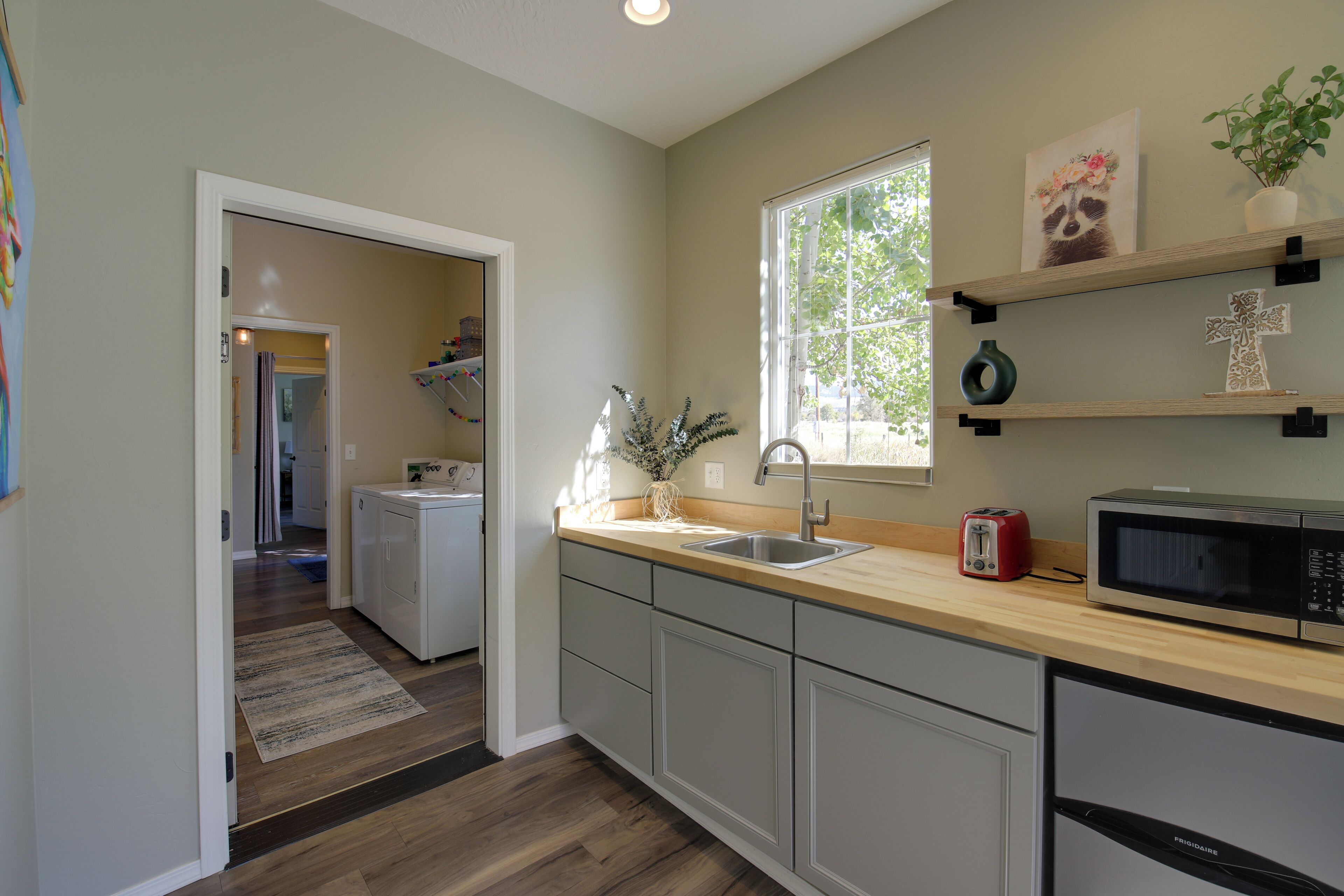 A kitchen with a wooden countertop, a sink, a microwave, and a toaster. There is a window with a view of trees outside.