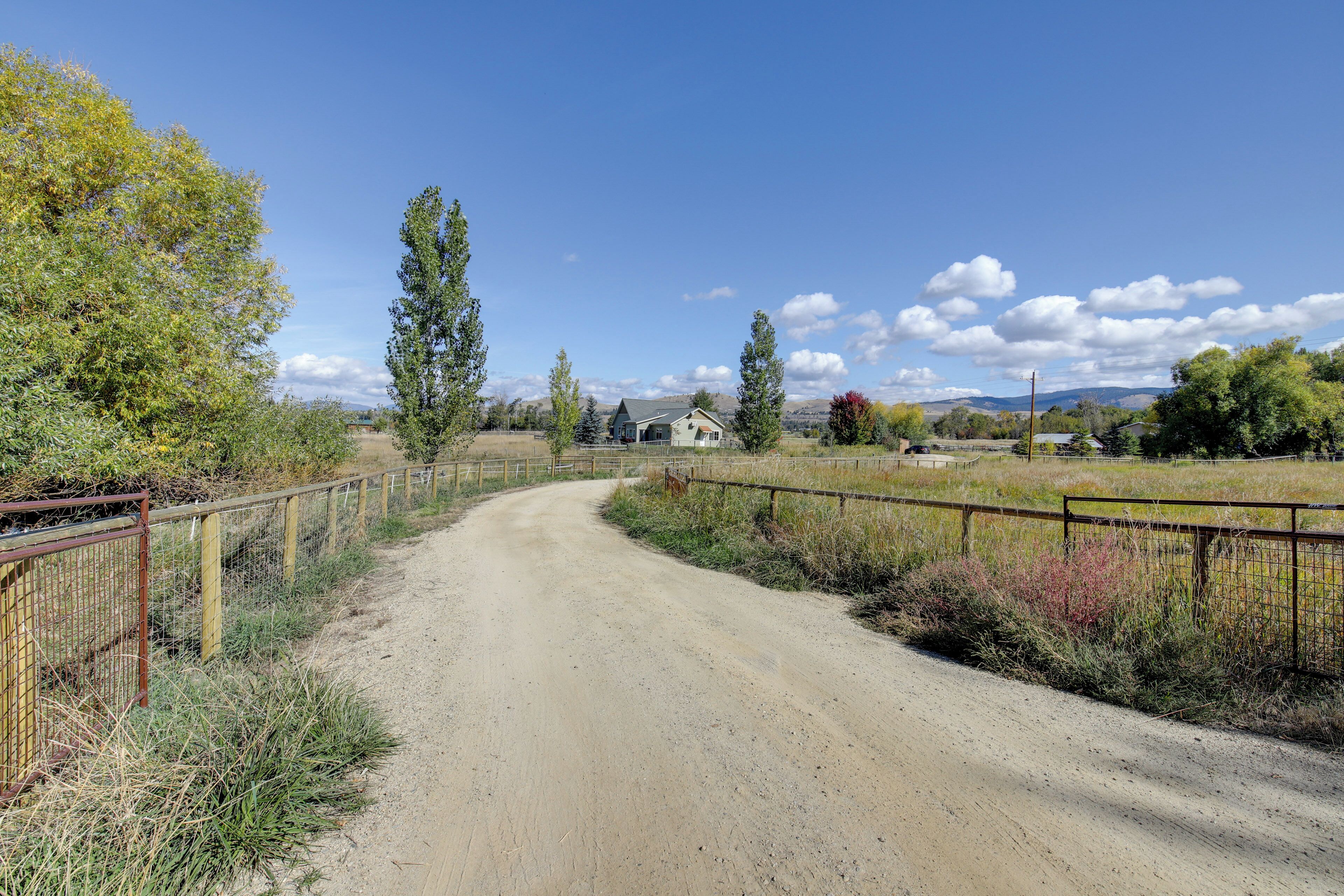 Un chemin de terre qui traverse la campagne et mène à une maison entourée de clôtures et de végétation.