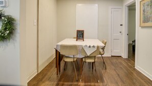 Un coin repas avec une table dressée pour quatre personnes, une porte blanche et un tableau encadré au mur.