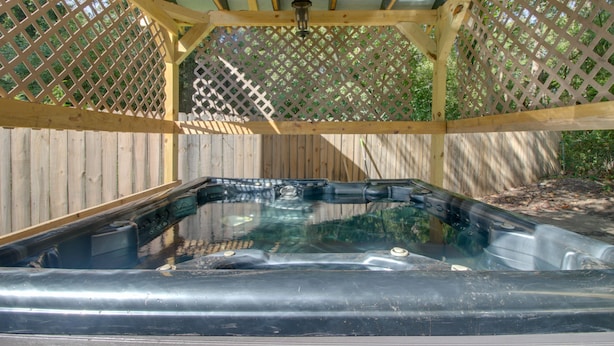 Un bain à remous installé sous une pergola en bois dont les côtés sont recouverts d’un treillis.
