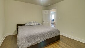 Une chambre à coucher avec un lit, un plancher en bois et une porte blanche donnant sur une autre pièce.